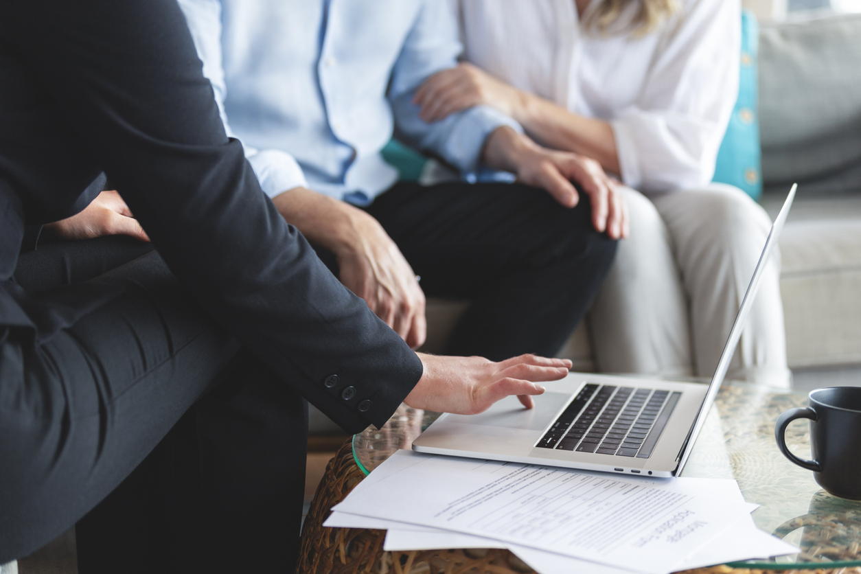 Mature couple meeting investments and financial advisor at home. The advisor is using a laptop.