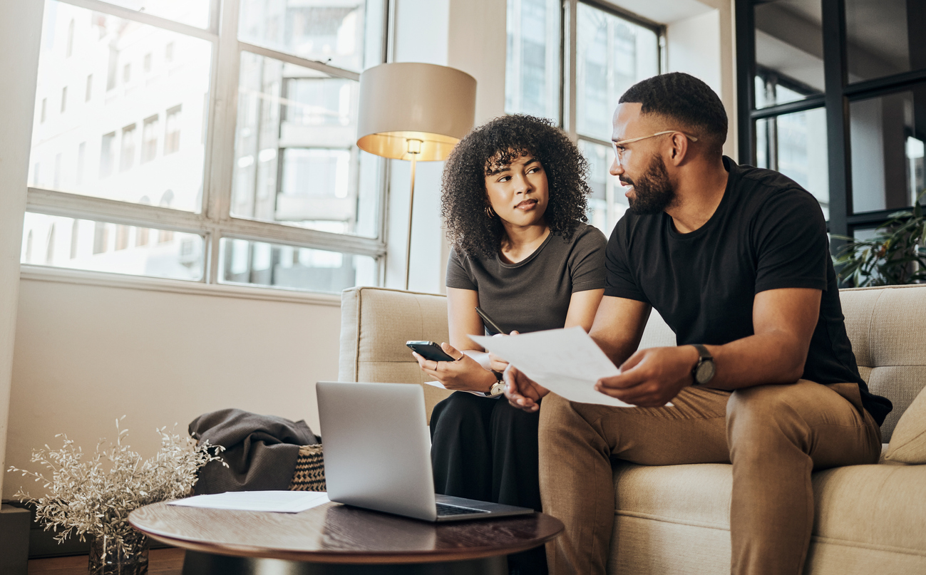 Finance, budget and couple on sofa with laptop, documents and paperwork for fintech in living room of home. Accounting, online banking and bank payment on mortgage, black woman and man in apartment.