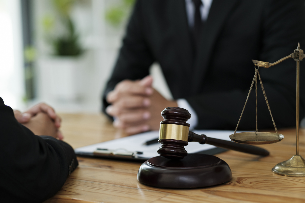 Attorney of lawyer discussing and consulting client about his offense, explaining cases, giving advise for going to courtroom with judge gavel and scale of justice on the table.