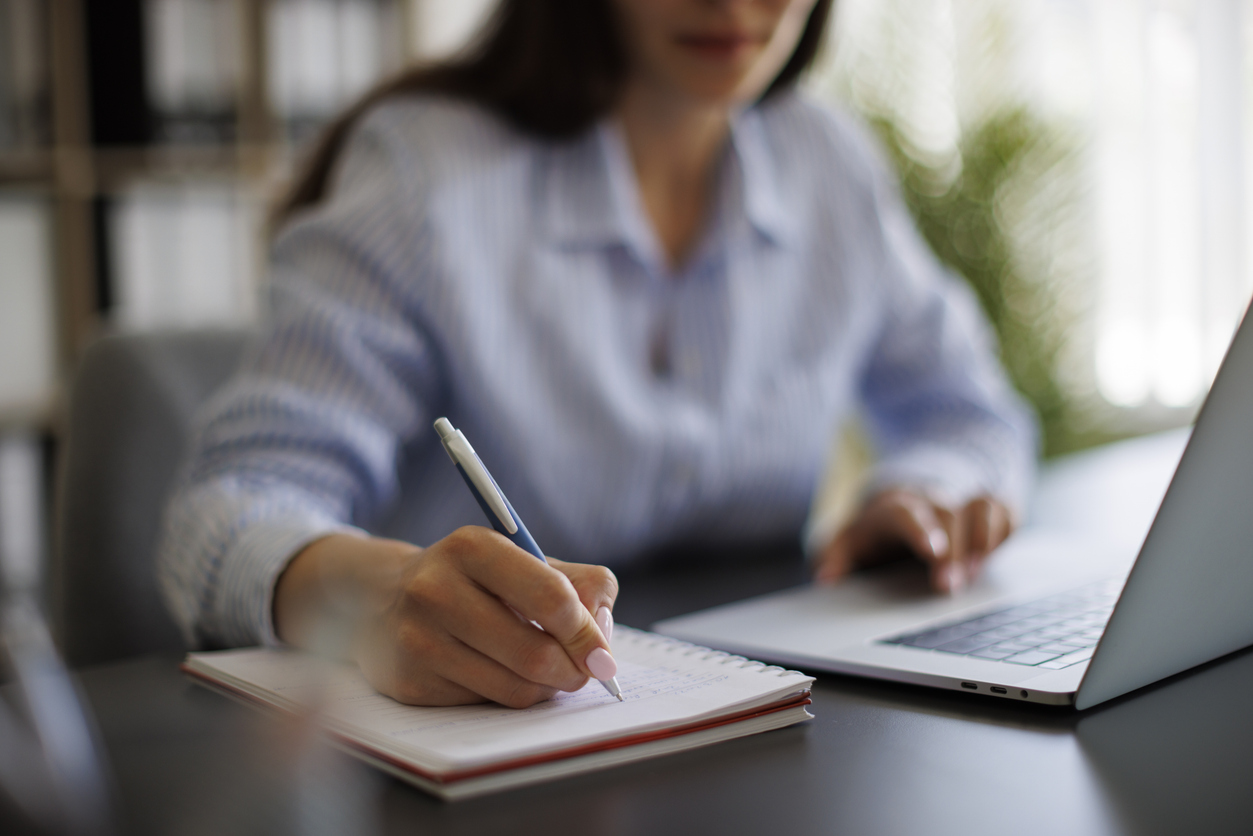 Businesswoman taking notes in notebook while working on laptop in the office