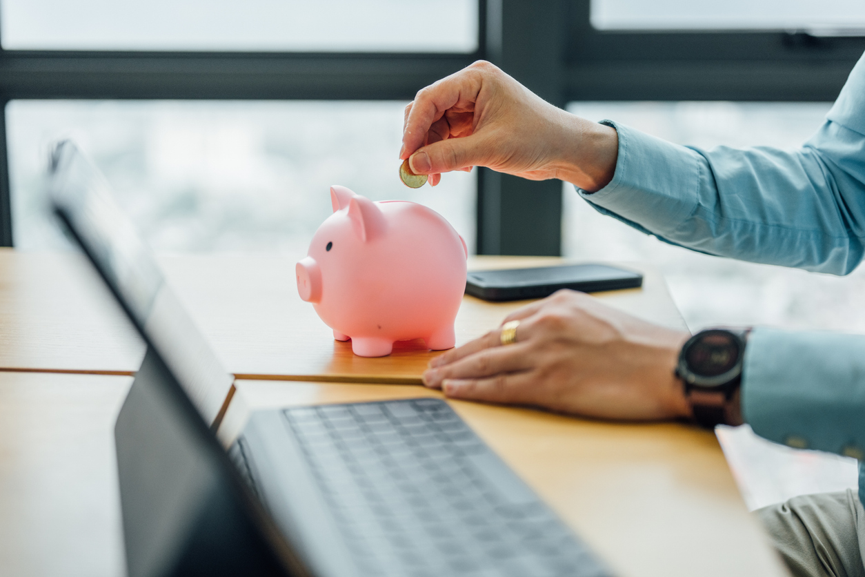 Anlawyer puts a gold coin into a piggy bank in the office — a concept of saving and investment.