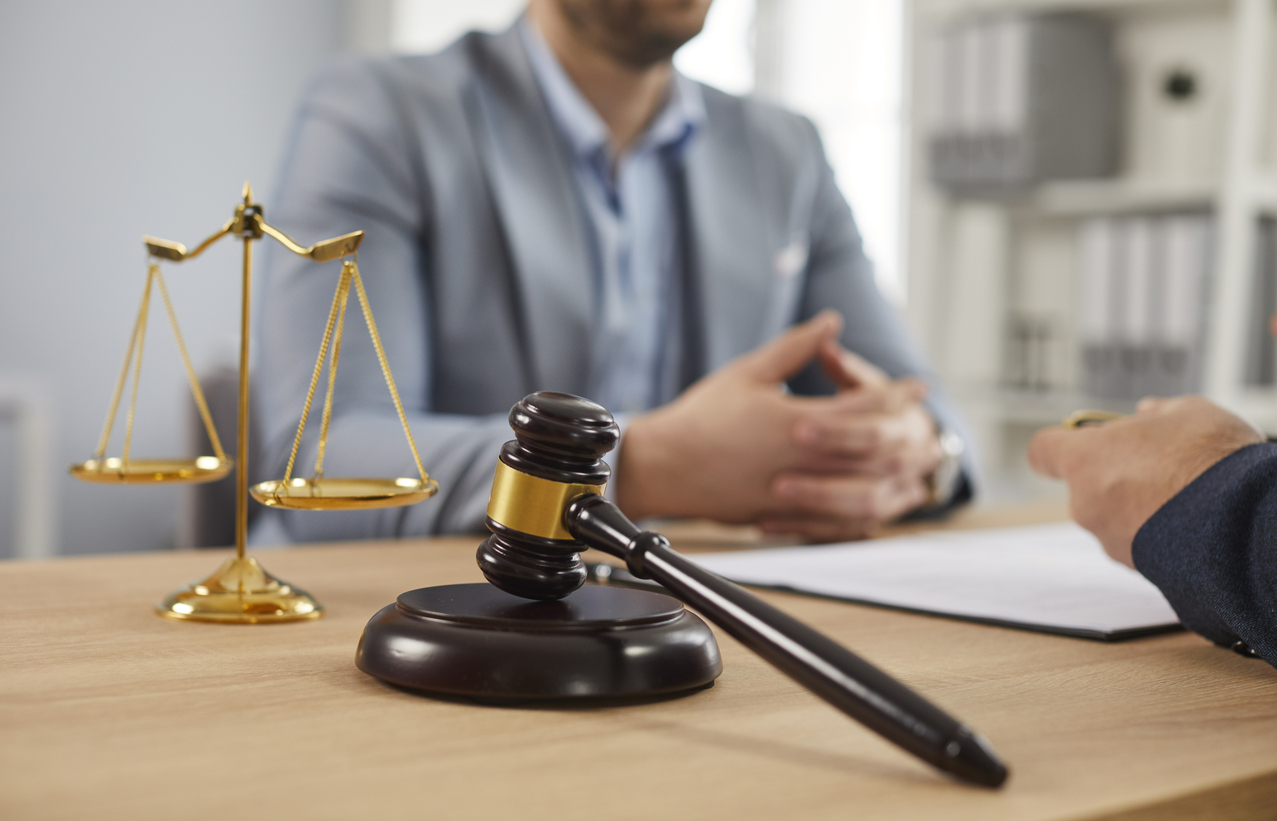 Close up of photo of a male lawyer working on his workplace in office on a wooden table with a judge's gavel and scales in the foreground. Legal law and advice concept. Selective ficus.