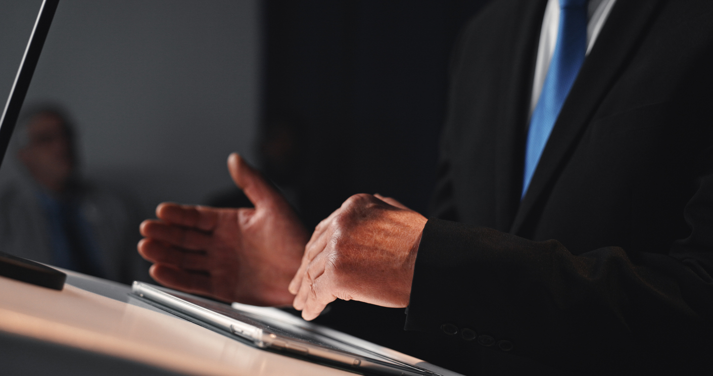 Politics, presentation and hands at podium with tablet, campaign or PR speech for election. Press conference, dark and ambassador in auditorium with tech, address or public relations for government.