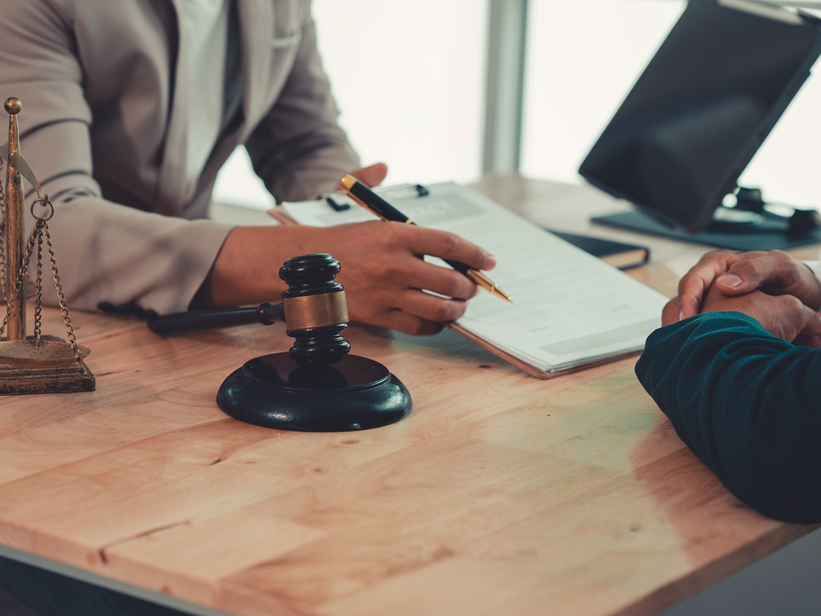 Lawyer holding pen and explaining legal contract terms on clipboard to client during consultation in law firm.