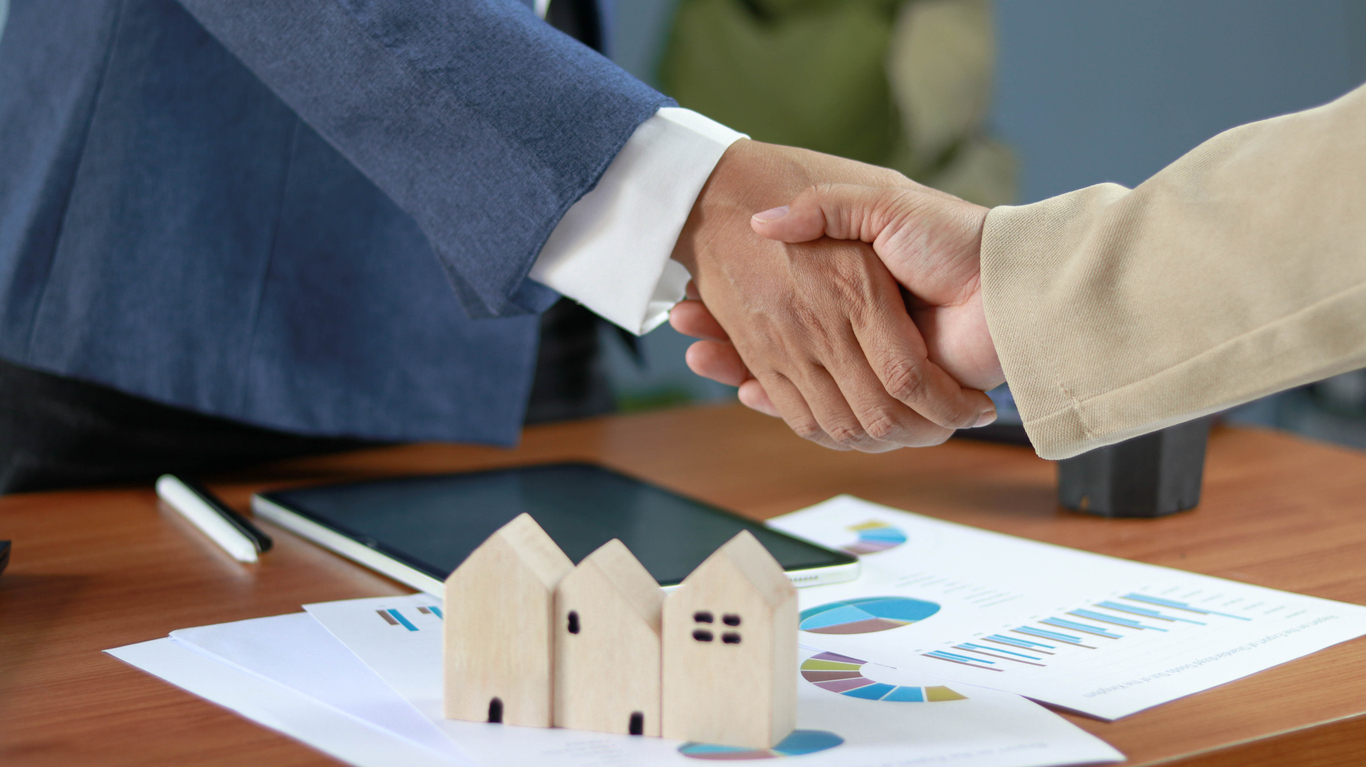 Business handshake over real estate investment documents with model houses, symbolizing property deals, partnership, mortgage agreement, home buying, financial planning, and successful negotiation